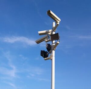 Multiple security cameras on a pole with a clear blue sky backdrop.